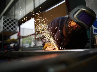 Un soudeur travaille sur un métal, produisant des étincelles brillantes. Il porte un casque de protection et des lunettes de sécurité, concentré sur sa tâche dans un atelier.