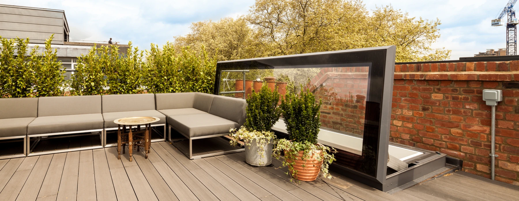 Terrasse spacieuse avec un salon moderne en teintes neutres, une table basse élégante et des plantes en pots, sous un ciel nuageux.