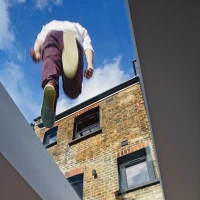 Un homme en train de sauter à l’intérieur d’un espace moderne avec un plafond vitré, laissant apparaître un mur en briques à l’extérieur.