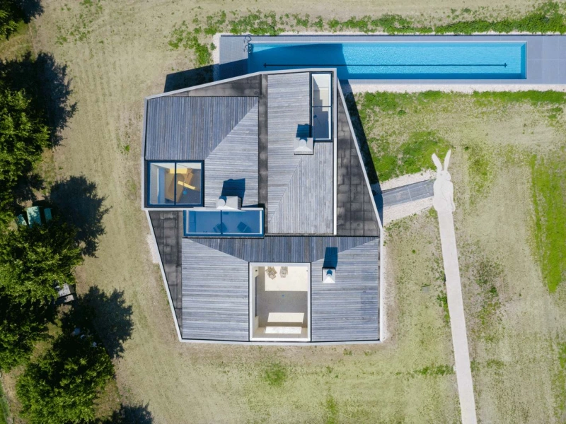 Birds eye view of a house with a pool attached to it. The surrounding areas is green fields.