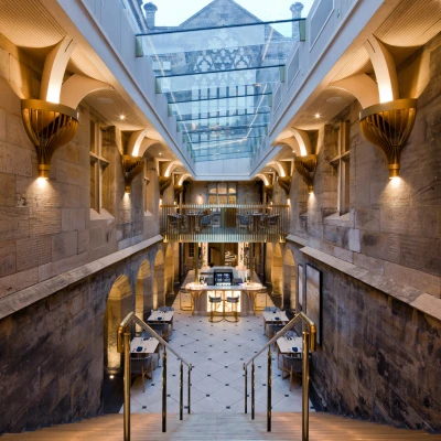 A grand stairway leads down into a stylish interior space featuring stone walls and warm lighting. A glass ceiling allows natural light to illuminate the area, which includes elegant tables and modern décor.