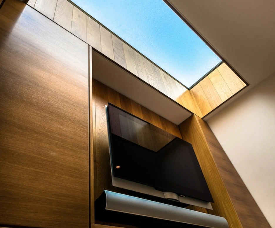 A wooden wall with a mounted television and soundbar underneath a skylight that reveals a blue sky.