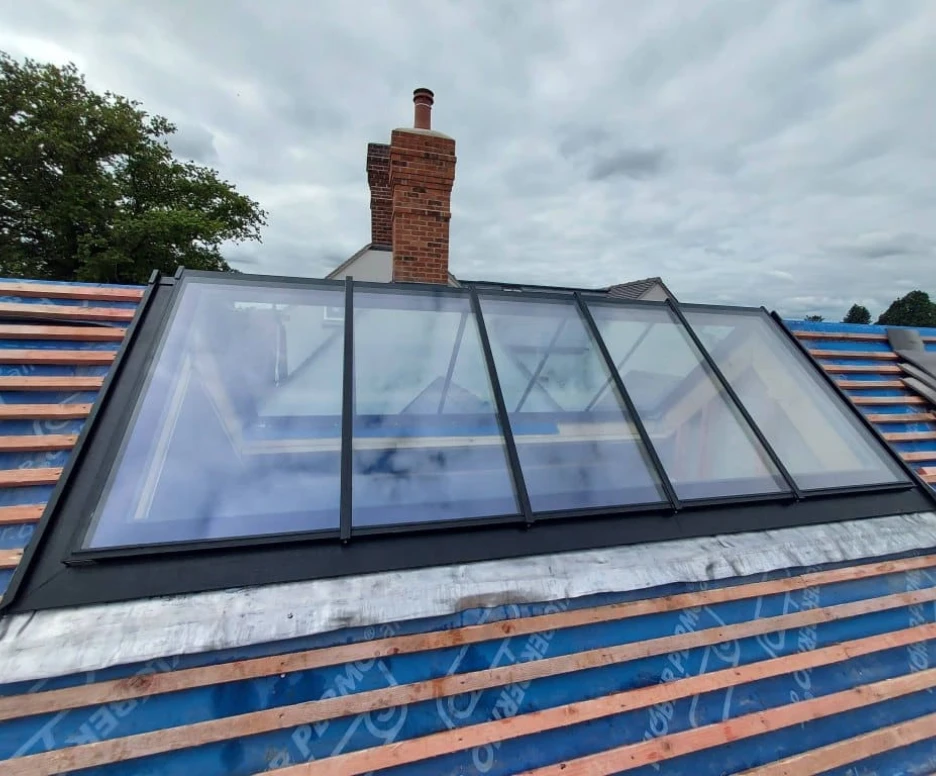 A newly installed skylight with multiple panels on a sloped roof, showcasing a cloudy sky reflected in the glass. A chimney is visible in the background.