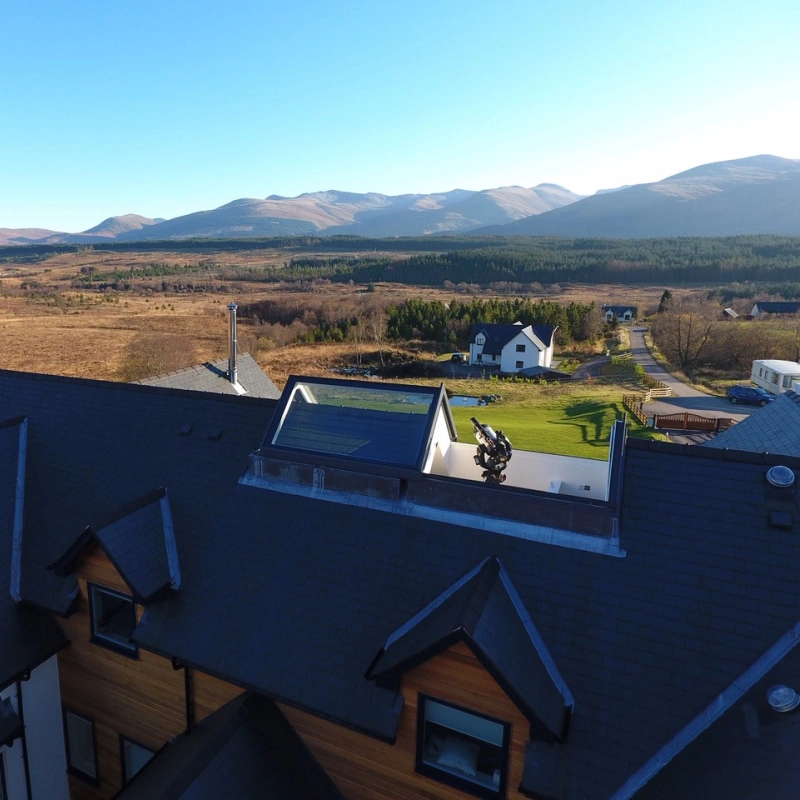 Shows a house with a telescope coming through the bespoke rooflight being about to see the surrounding areas of grass and mountains.
