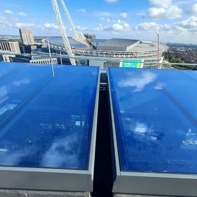 Two large blue skylights on a rooftop with a view of a stadium in the background. The sky is partly cloudy, and the city skyline is visible in the distance.