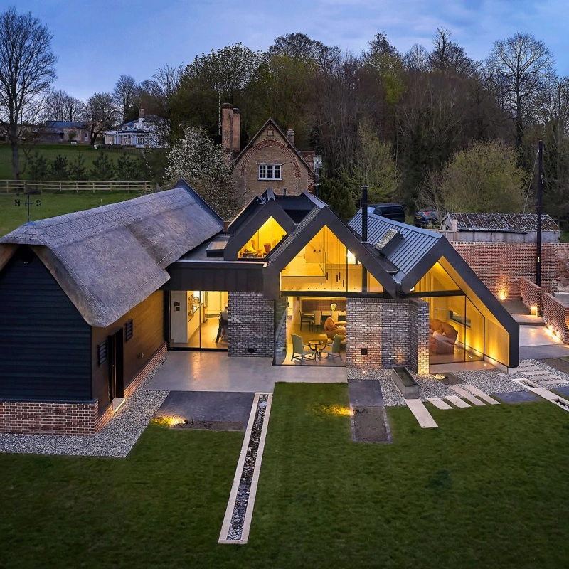 Shows a drone shot of a big house with lots of glass showing inside of the house