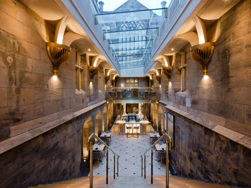 Inside a golden brown building with large stairs leading down. There is a multipart skylight which lets natural light in