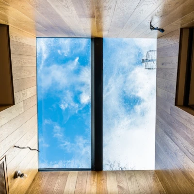 A flat ceiling with wooden panels and a large rectangular skylight showing a cloudy blue sky. Rainwater droplets are visible on the skylight's surface.