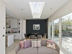 flat skylight installed in modern white living room with black back wall. A sofa and dining table and chairs take up the space
